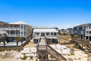 A beachfront property with multiple buildings, a swimming pool, and a wooden deck leading to the beach.