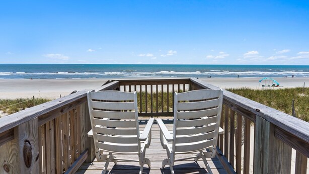 A wooden deck with two white chairs facing a beach. - Chasing Sunrises | Newly Rebuilt Luxury Oceanfront Retreat (Ocean Isle Beach)
