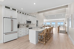 A spacious kitchen with white cabinetry, a large island, and a dining area with wicker chairs.