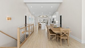 A modern kitchen with a central island, wooden dining table, and chairs. - Chasing Sunrises | Newly Rebuilt Luxury Oceanfront Retreat (Ocean Isle Beach)