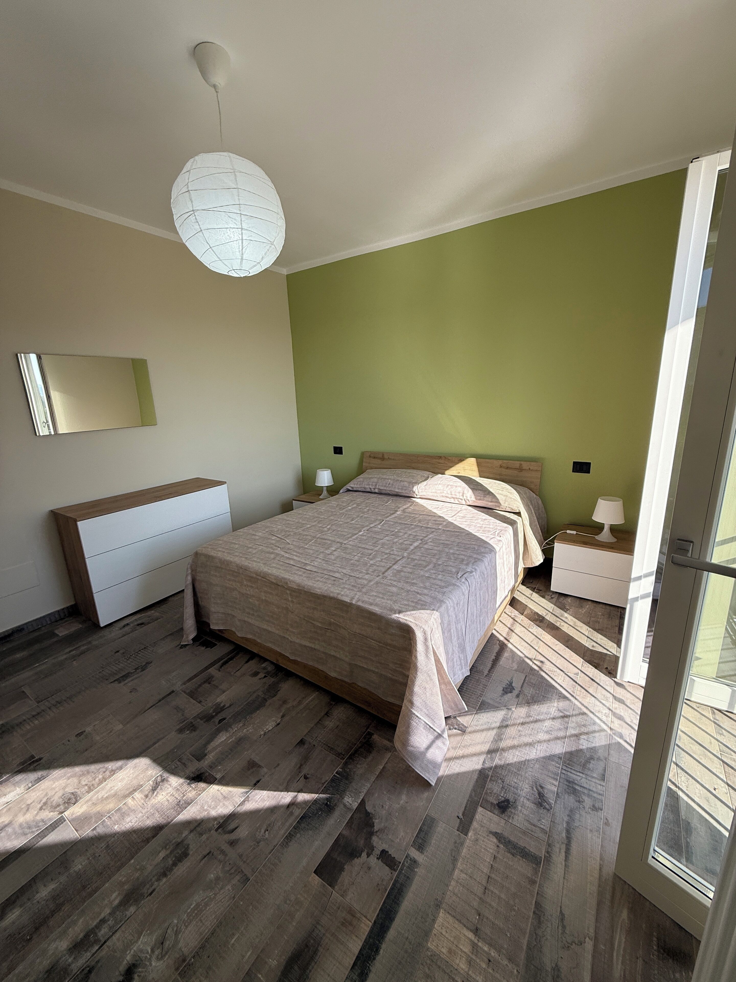 A bedroom with a bed, bedside tables, a mirror, and a hanging light fixture.