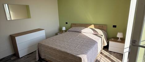 A bedroom with a bed, bedside tables, a mirror, and a hanging light fixture.
