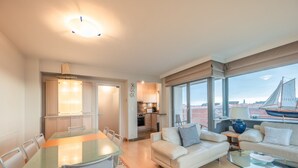 A modern living room with a glass dining table, a sofa, and a coffee table. There is a view of a sailboat through large windows. - Apartment in Knokke-heist With Sea Views (Knokke-Heist)