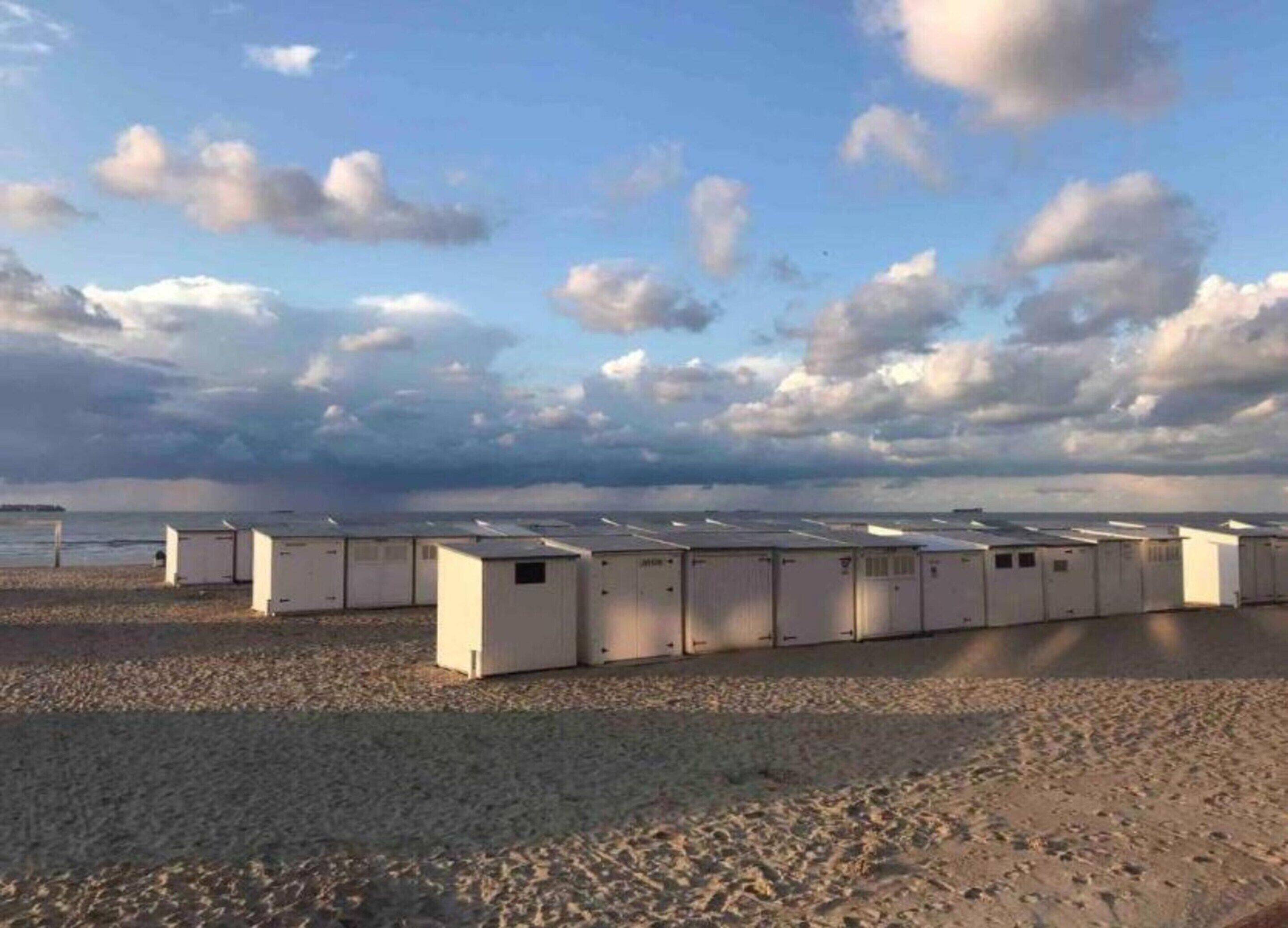 Une rangée de cabines préfabriquées, avec une plage et l’océan en arrière-plan.