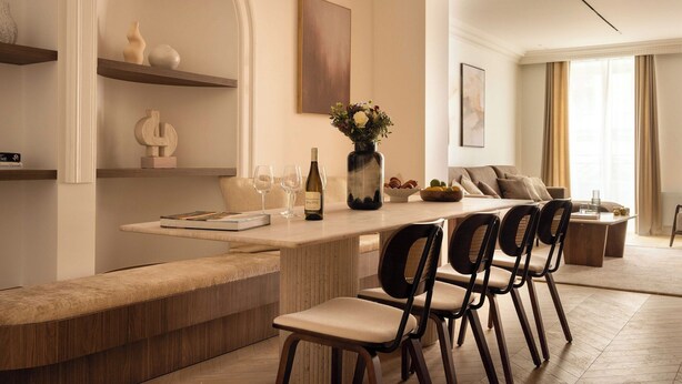 A modern living room with a built-in bench, a dining area with chairs, a vase with flowers, and a wine bottle.