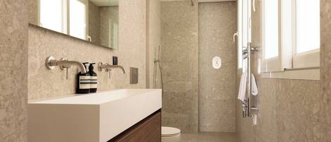 A modern bathroom with a marble countertop, a shower, and a toilet.
