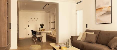 A modern living room with a brown sofa, a wooden coffee table, and a dining area with chairs and a table.