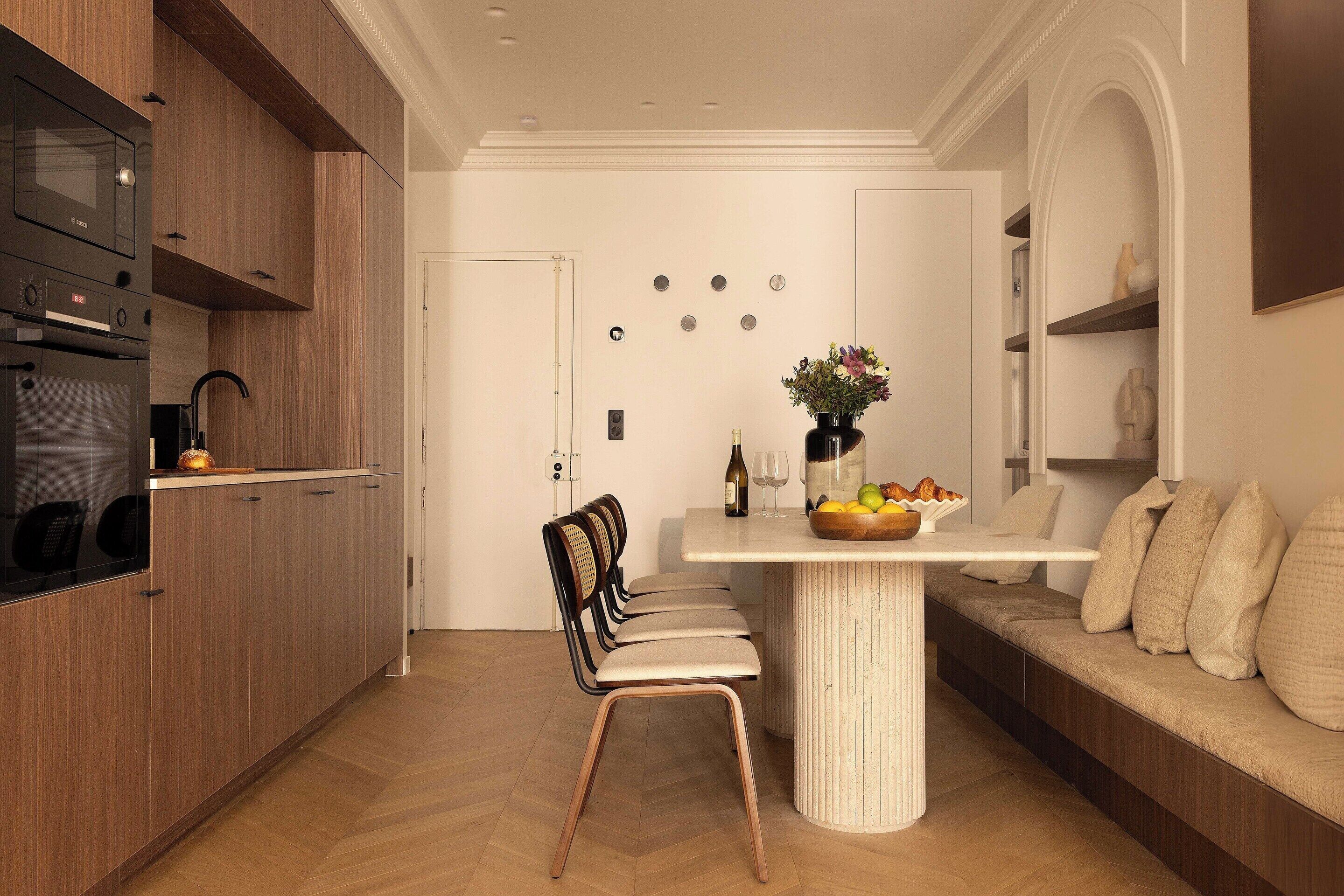 A modern kitchen with wooden cabinets, a built-in oven, and a dining area with a white table and chairs.