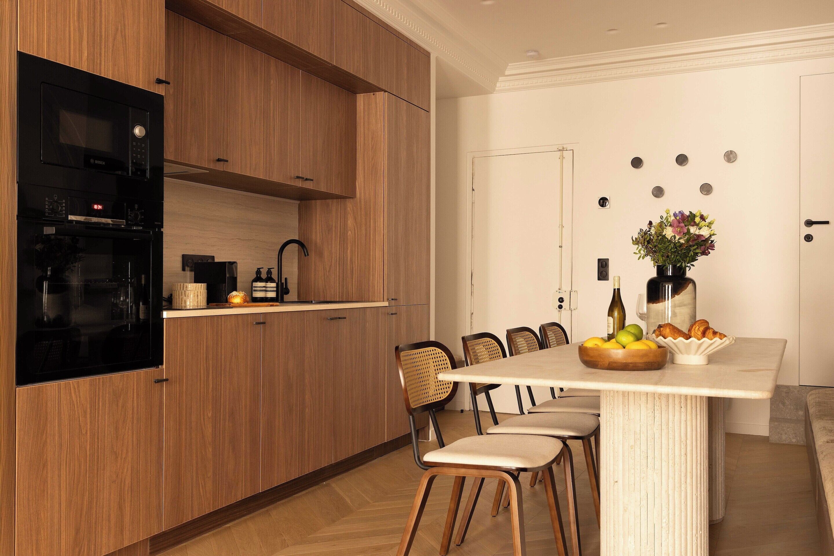 A modern kitchen with wooden cabinets, a built-in oven, and a dining area with a white island and chairs.