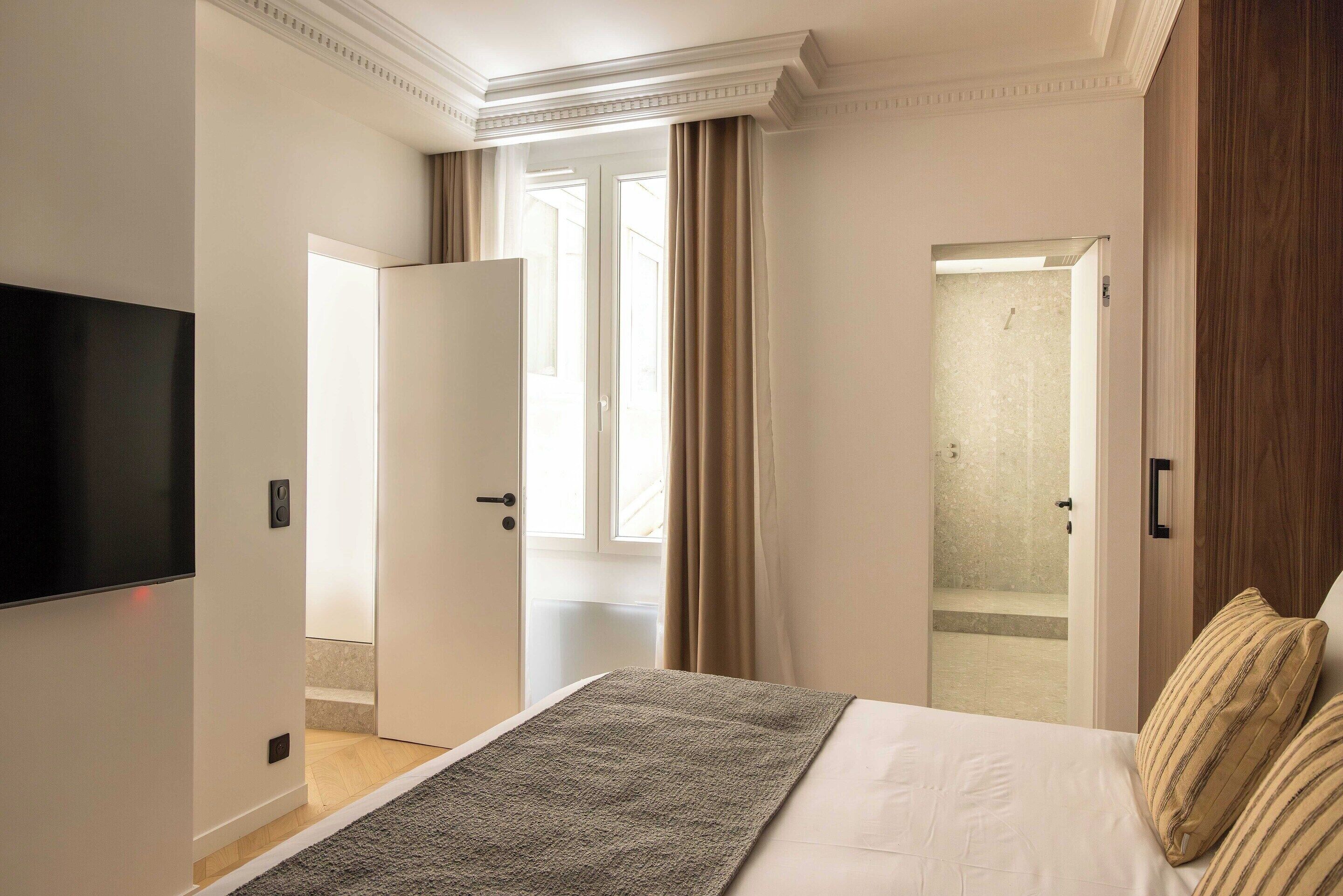 Una habitación de hotel con cama, televisión, ducha y puerta que da a otra habitación.