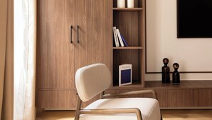 A modern living room with a wooden wardrobe, a white armchair, and a flat-screen TV mounted on the wall.