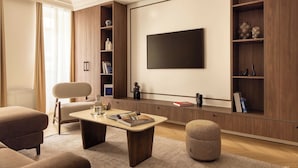 A modern living room with a flat-screen TV mounted on the wall, a sofa, a coffee table, and built-in wooden shelving with decorative items.