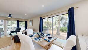 Comedor con mesa dispuesta para cuatro personas, ventilador de techo y ventanas amplias con cortinas.