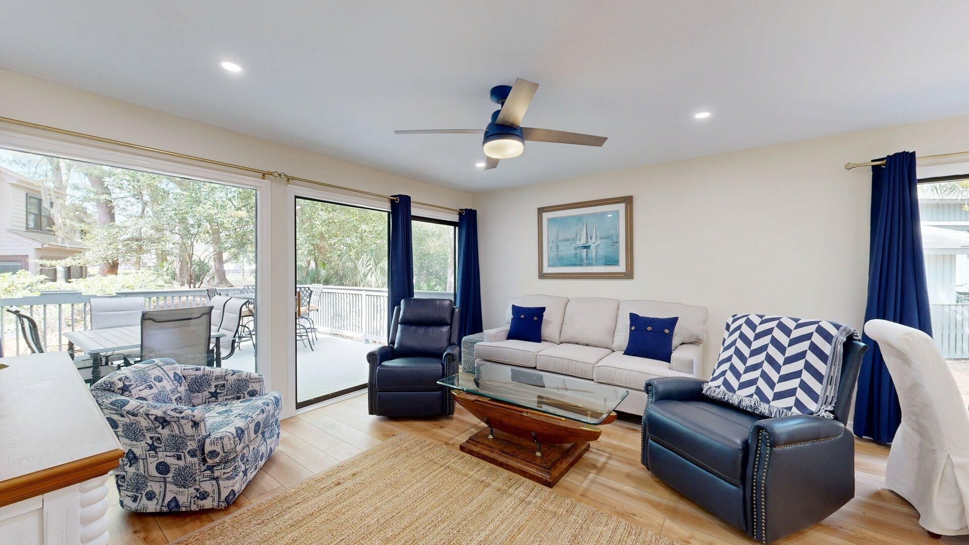 A spacious living room with a sofa, armchairs, a coffee table, and a ceiling fan.