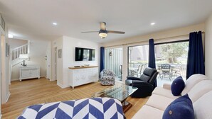 Una sala de estar moderna con una mesa de centro de vidrio, un sofá, un sillón estampado y un televisor montado en la pared.