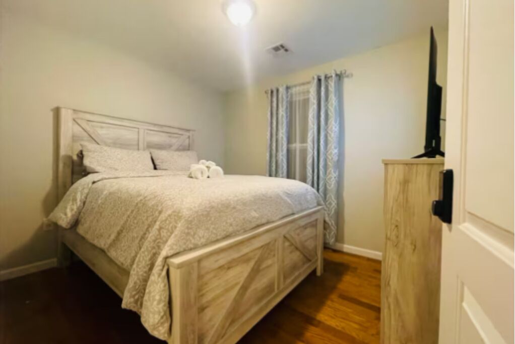 Une chambre à coucher avec un lit en bois, une table de chevet et un téléviseur posé sur un meuble en bois.