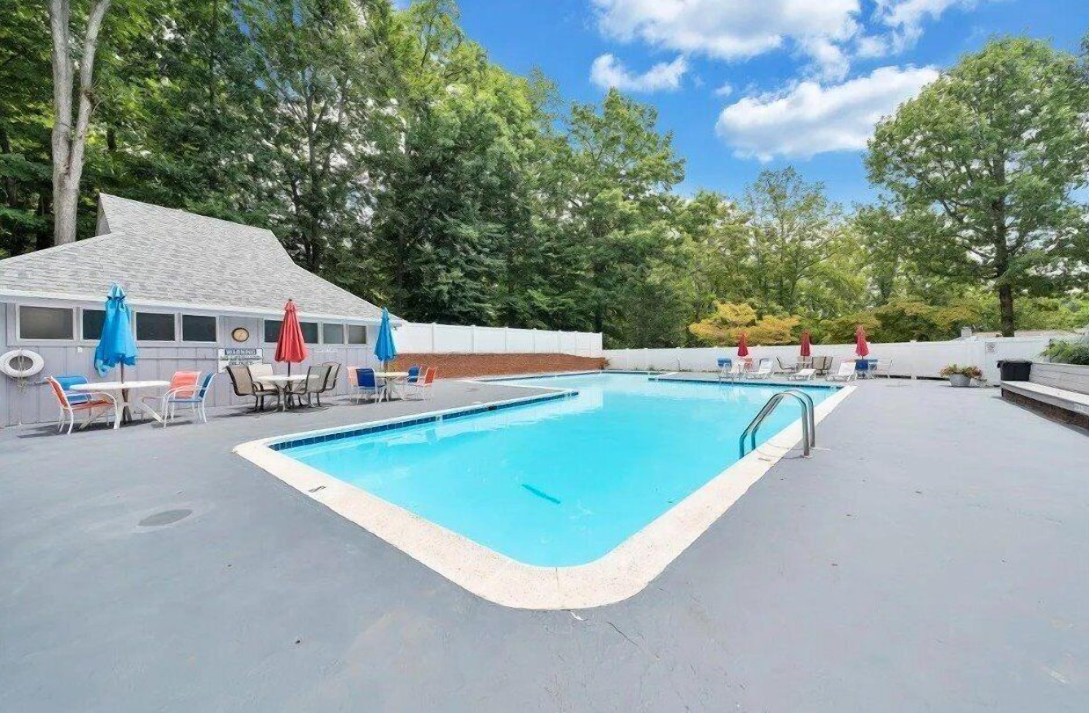 A rectangular pool with a white deck, surrounded by lounge chairs and umbrellas.