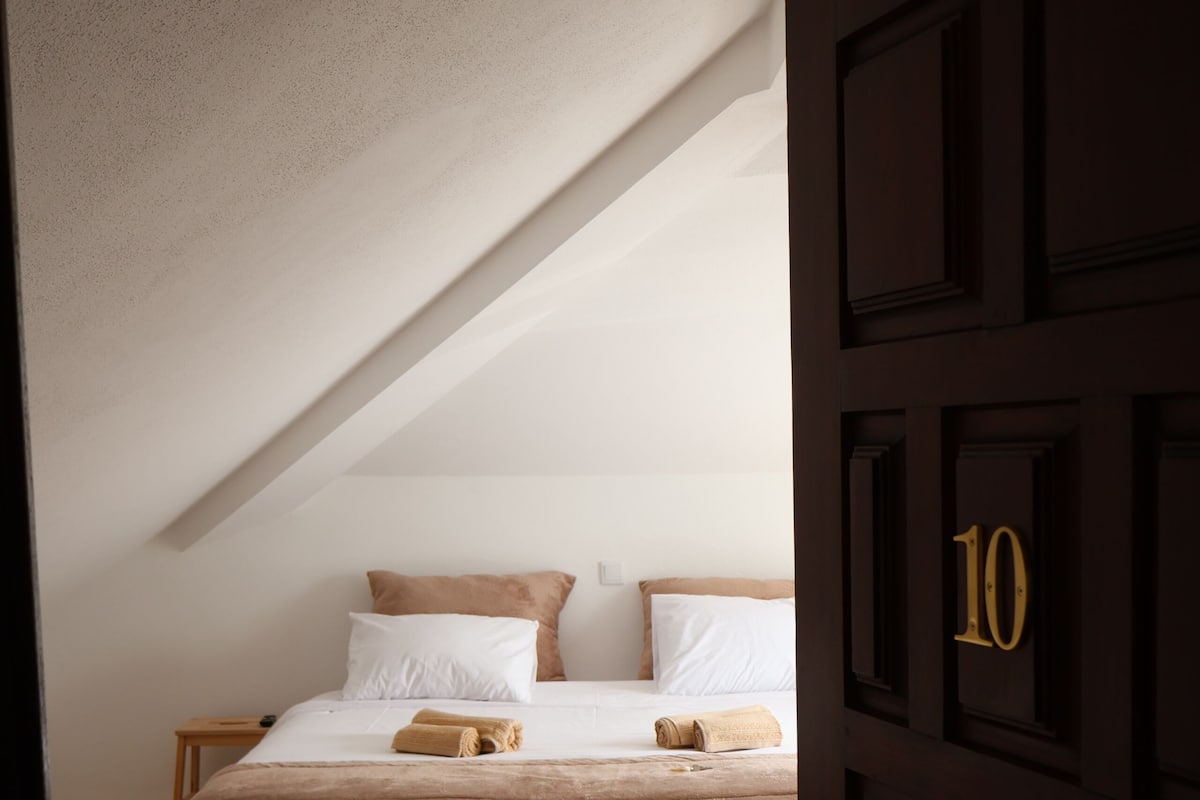 A bedroom with a wooden floor, a bed with white bedding, and a door with the number 10.