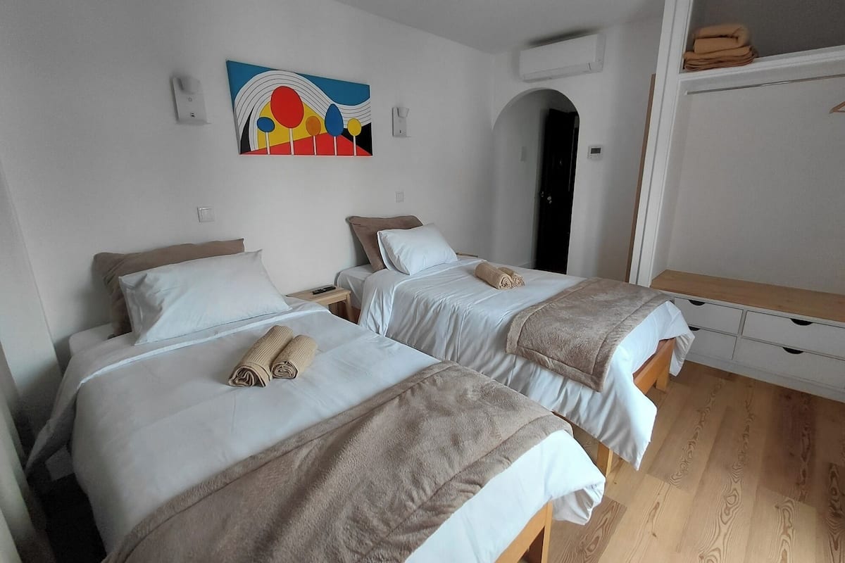 A hotel room with two beds, each with a white duvet and a brown blanket, a painting on the wall, and a wooden floor.