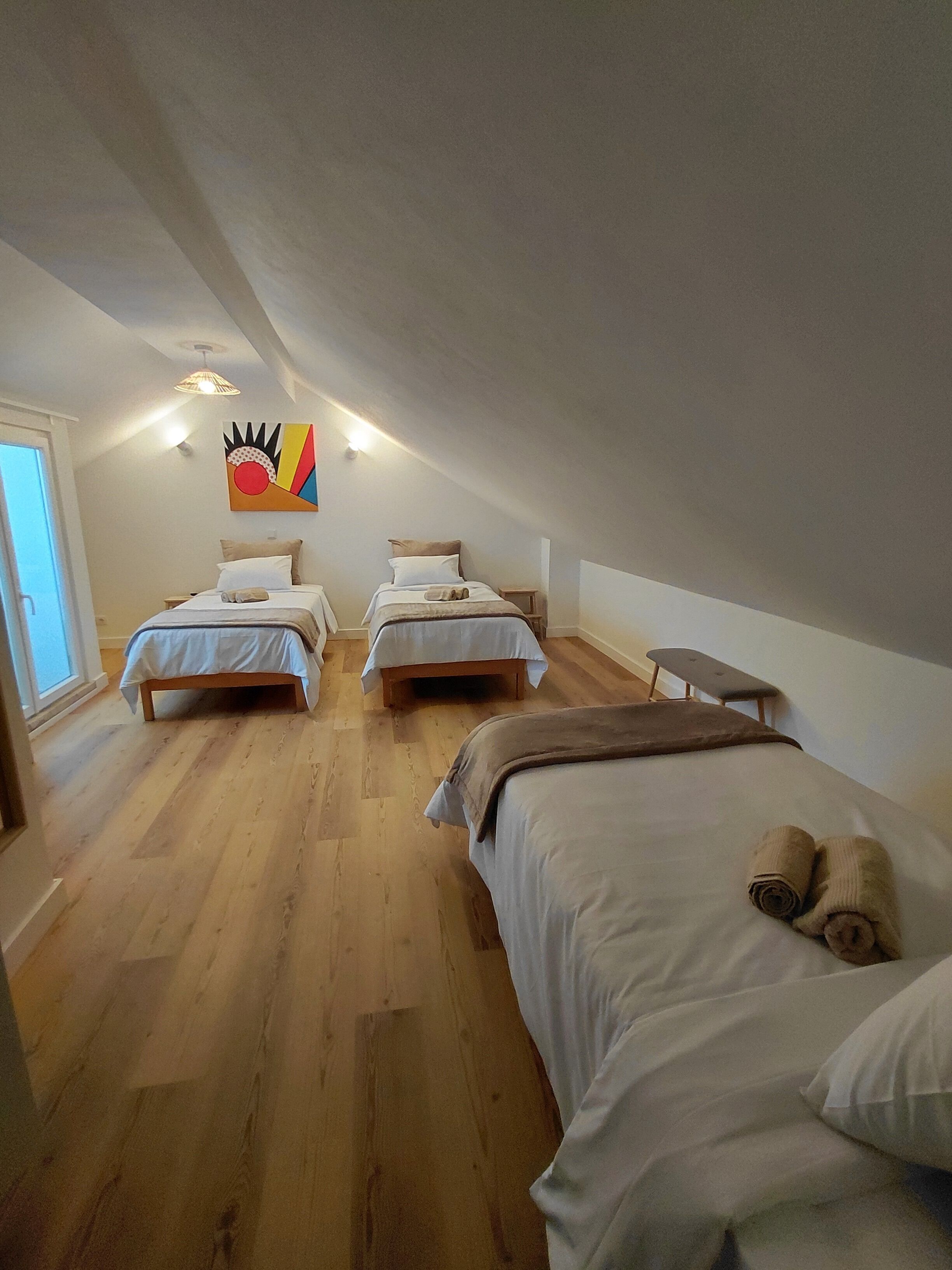 A room with two beds, a bench, and a colorful artwork on the wall.