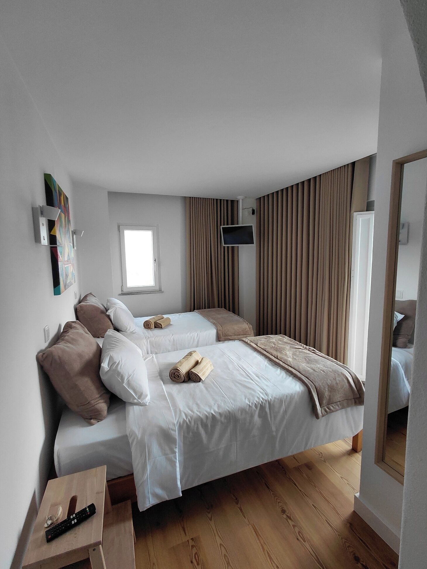 A hotel room with two beds, a TV, a window, and a wooden floor.