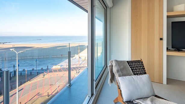 Ein modernes Zimmer mit großem Fenster und Meerblick, einem Holzschrank und einem Fernseher auf einer Ablagefläche.