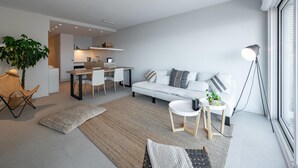 Ein modernes Wohnzimmer mit einer Couch, einem Couchtisch und einem Essbereich mit Stühlen, im Hintergrund eine Küche.