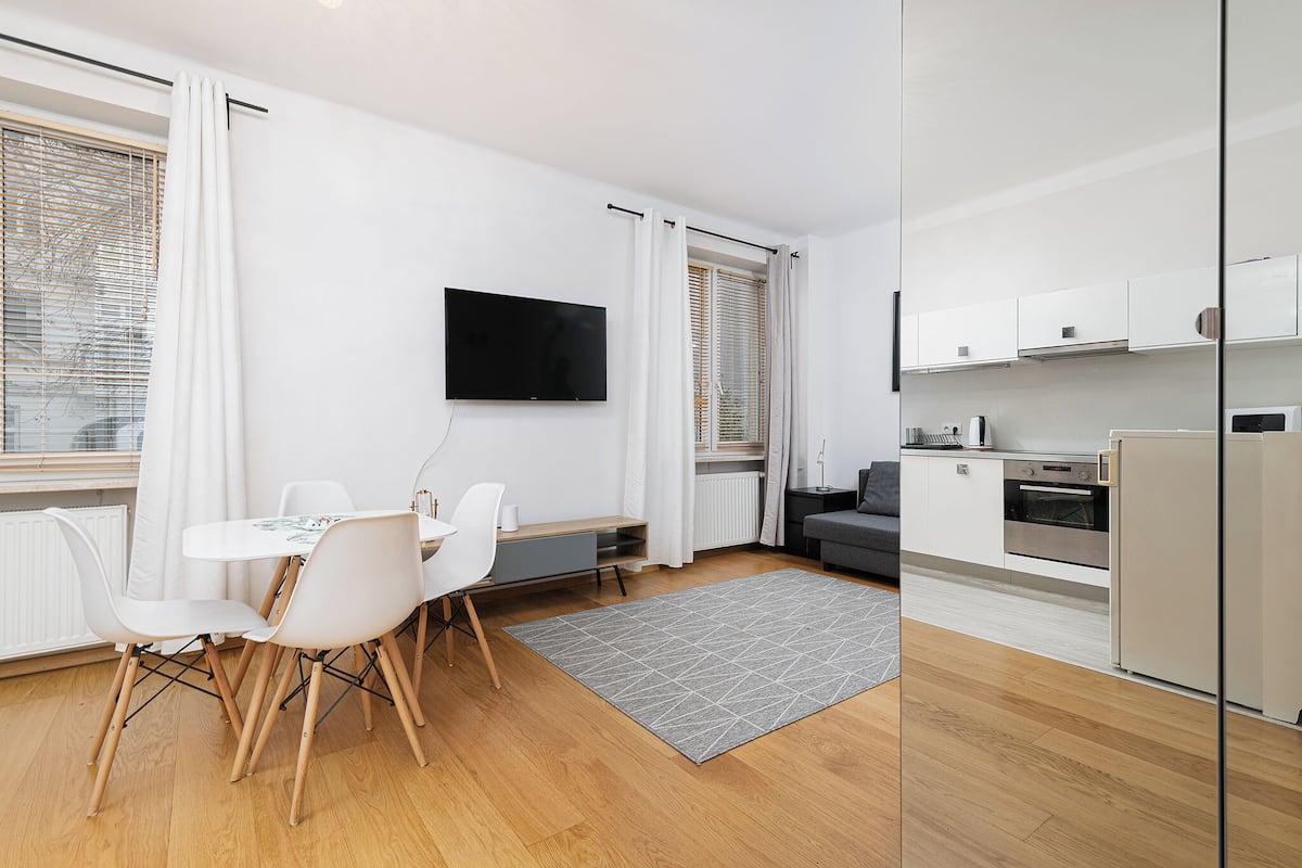 A modern apartment with a dining area, kitchen, and a TV mounted on the wall.