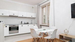 A modern kitchen with white cabinets, a built-in oven, and a dining area with a round table and four chairs. - RentPlanet - Apartament Chmielna (Warsaw)