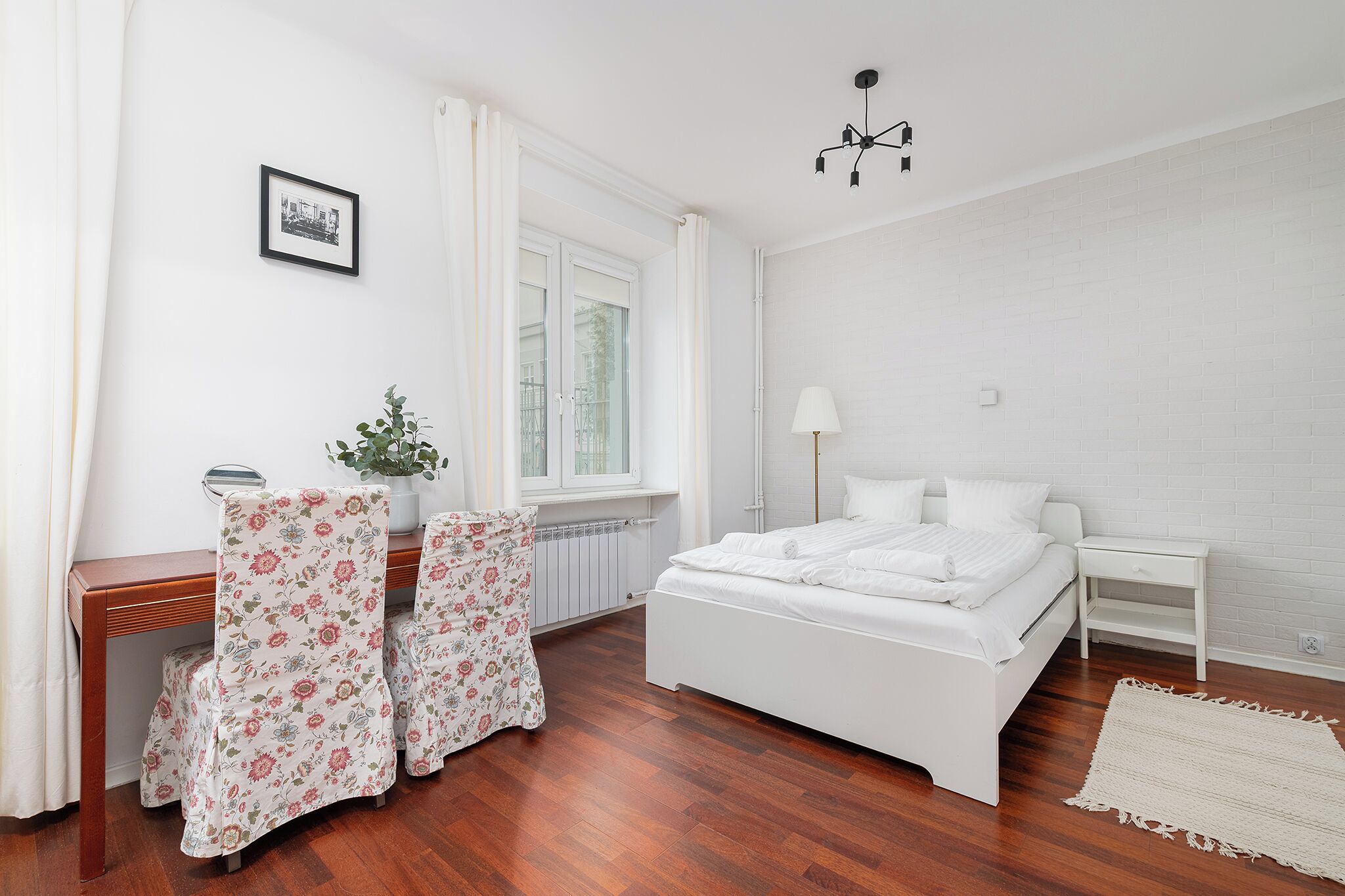 Une chambre à coucher avec un lit, une table de chevet, une chaise et une fenêtre avec des rideaux.