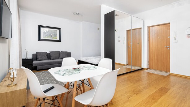 A modern living room with a sofa, a dining table with chairs, a TV, and a large mirror. - RentPlanet - Apartament Chmielna (Warsaw)