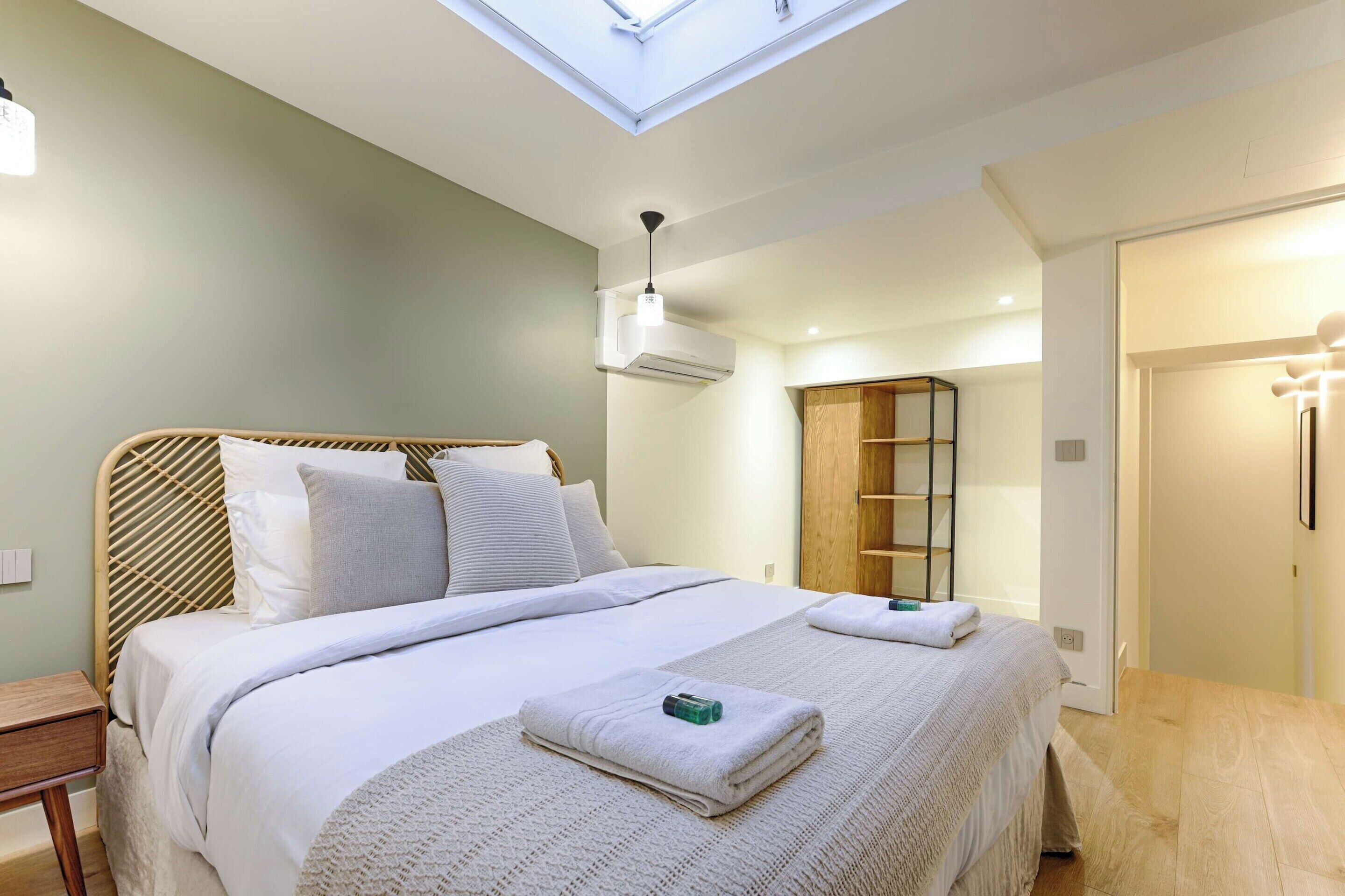 A modern bedroom with a skylight, a bed with white linens, a bedside table, and a wooden wardrobe.