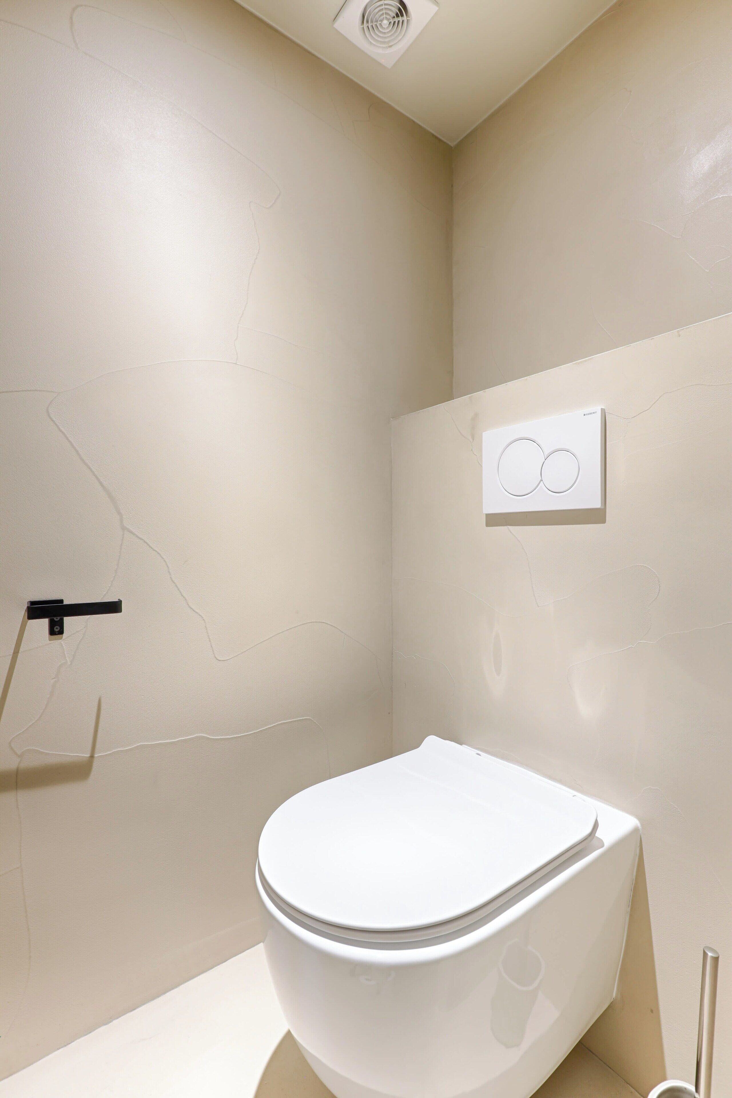 A modern bathroom with a white toilet, a visible water heater, and a wall-mounted control panel.