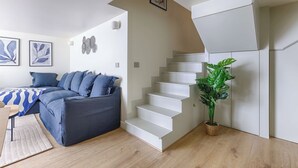 A modern living room with a grey sectional sofa, a staircase, and a potted plant. - Superb Air-conditioned Duplex - Bastille Le Marais (Paris)