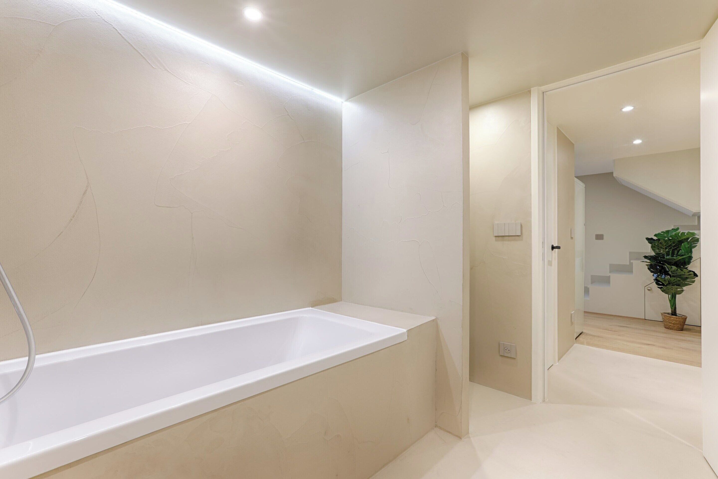 Ein modernes Badezimmer mit einer großen Badewanne, einer separaten Dusche und einer Zimmerpflanze im Hintergrund.