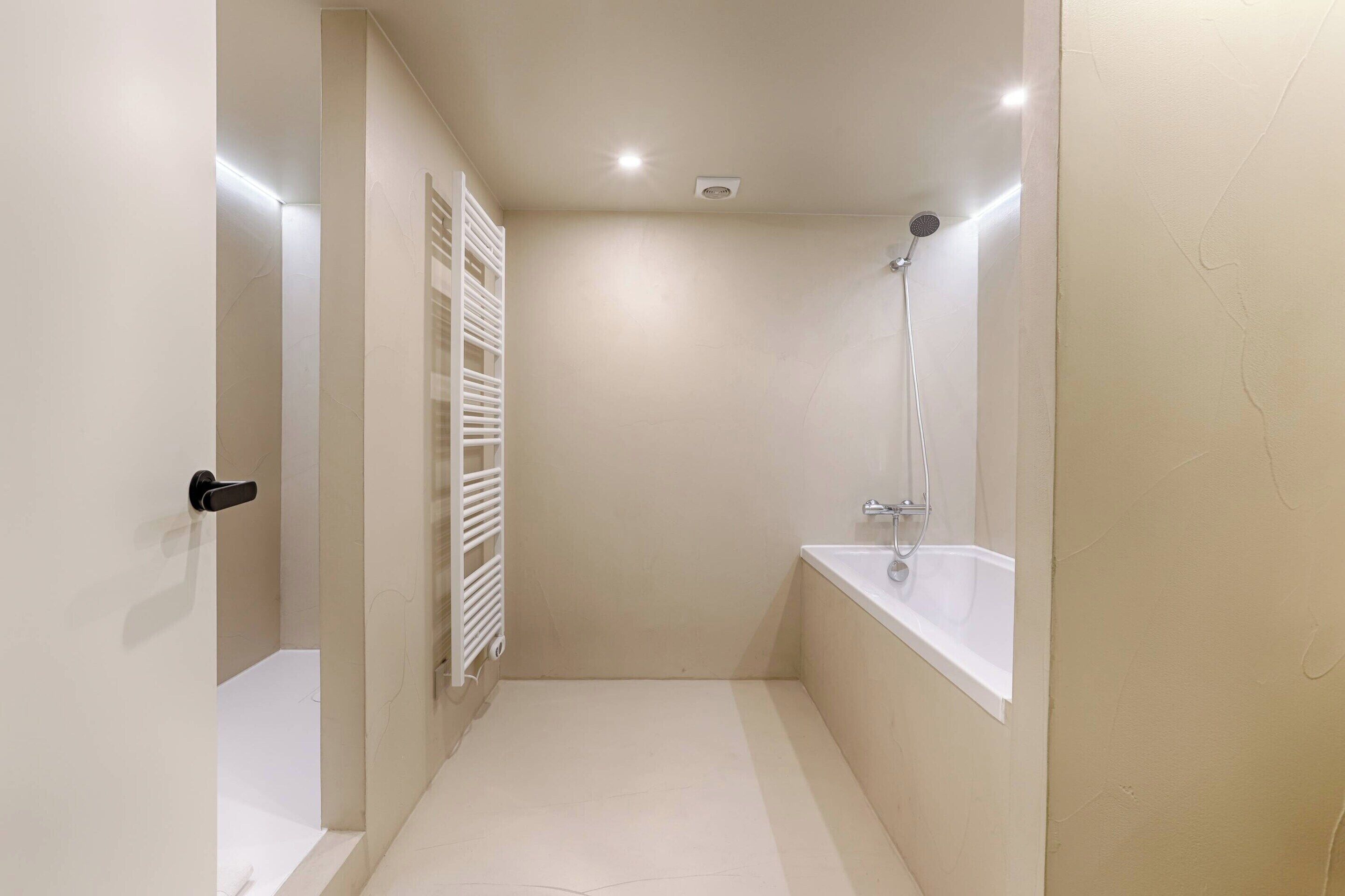 A narrow, well-lit bathroom with a shower, a toilet, and a sink.