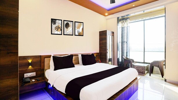 A modern hotel room with a large bed, bedside tables, a desk, and a view of the city. - Super Hotel O Somnath Formerly Hotel Somnath Tirth (Veraval)