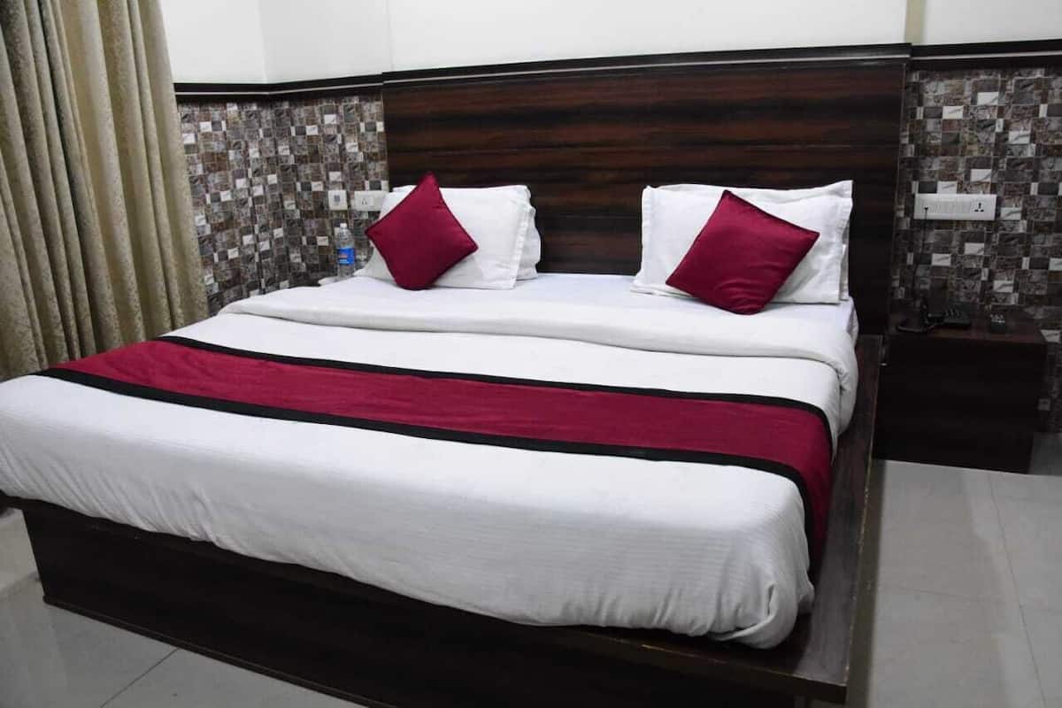 A neatly made bed with white and red bedding, a dark wooden headboard, and a tiled wall with a mosaic pattern.