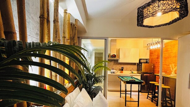 A modern living room with a sofa, a dining area, and a kitchen visible through an open door. - Cozy 1-bedroom apartment in pleasant Parañaque with AC (Parañaque)