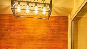 A dining area with a wooden wall, a table set for two, and three yellow stools. - Cozy 1-bedroom apartment in pleasant Parañaque with AC (Parañaque)
