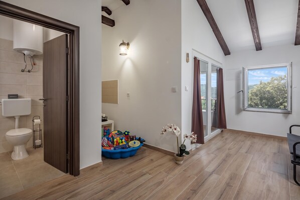 A spacious bathroom with a toilet, shower, and a sink. There is a window with curtains, and a wooden floor. - Harmony House Vito With Lovely Terrace (Lopar)