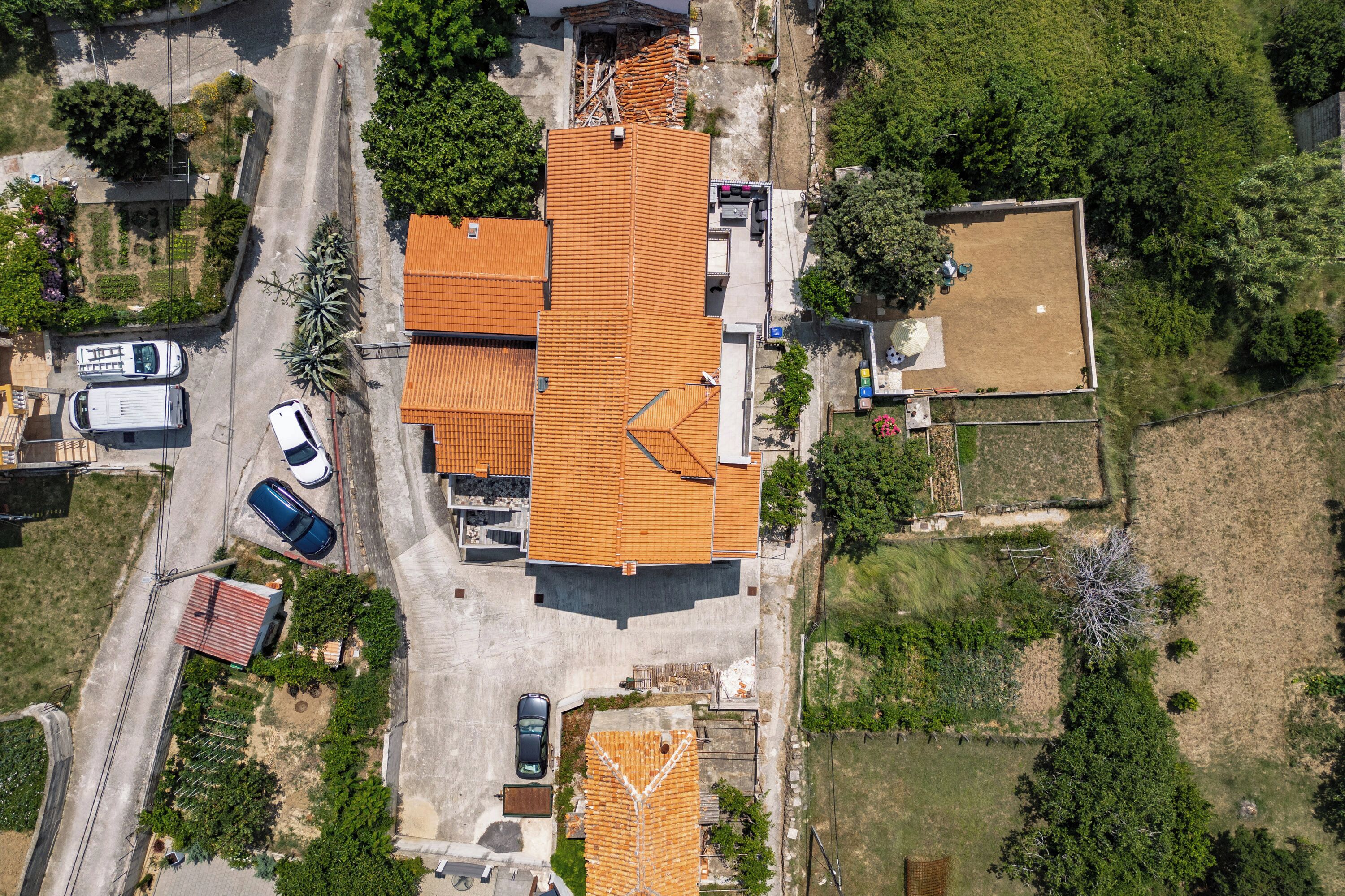 Vista aérea de una zona residencial con una casa de techo de tejas, un camino de acceso y zonas verdes adyacentes.