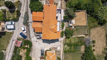 Vista aérea de una zona residencial con una casa de techo de tejas, un camino de acceso y zonas verdes adyacentes.