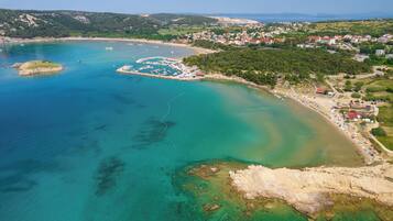An aerial view of a coastal area with clear waters, a marina, and a residential area with houses and greenery.
