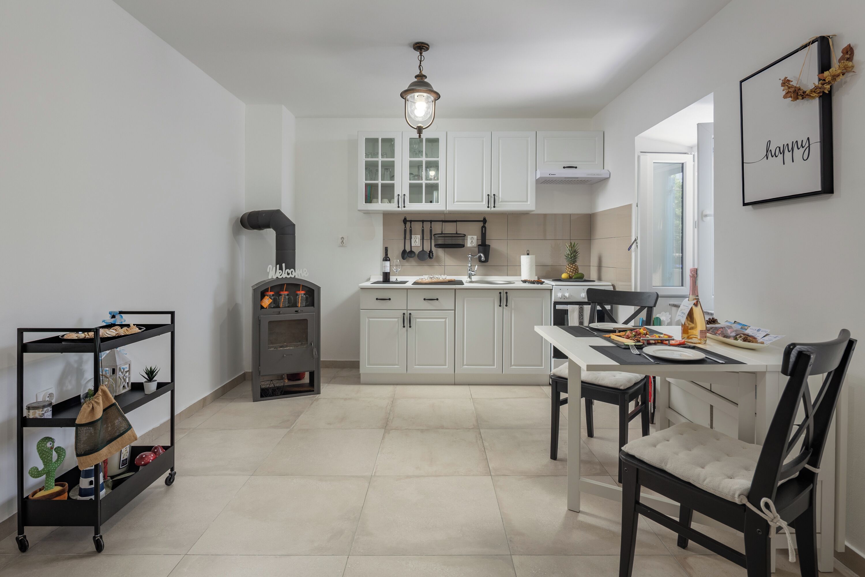 A modern kitchen with white cabinets, a dining area with a table and chairs, and a small cart with items.
