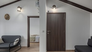 Uma sala de estar moderna com uma porta de madeira escura, um sofá cinza e uma cadeira com estrutura de metal.
