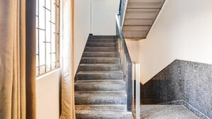 A staircase with a metal railing, leading to a landing with a textured wall. - Classic Q Rooms BTM Gopalan Ovation Mall (Bengaluru)