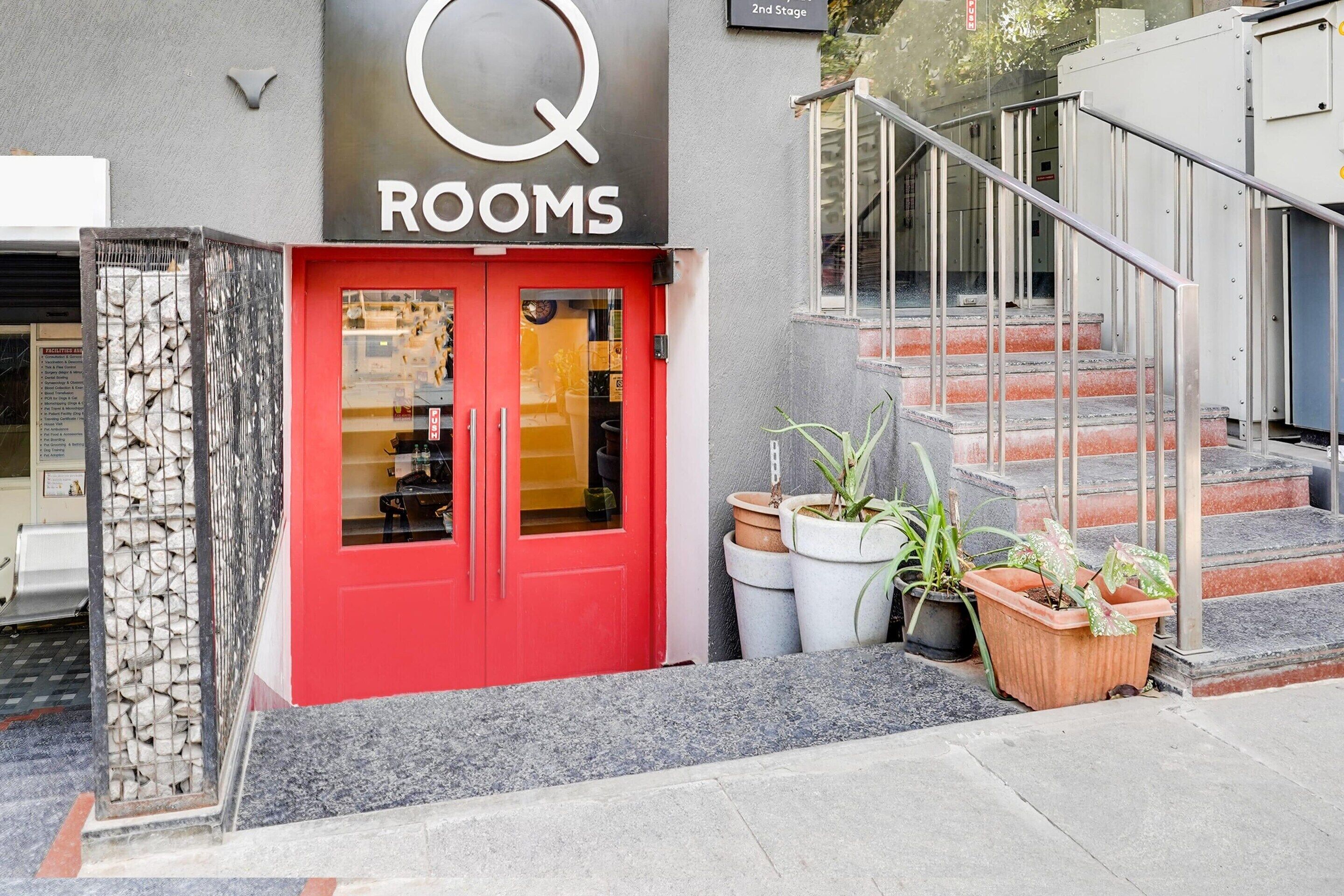 A building with a red door labeled "Q ROOMS" and a staircase leading to an upper level.