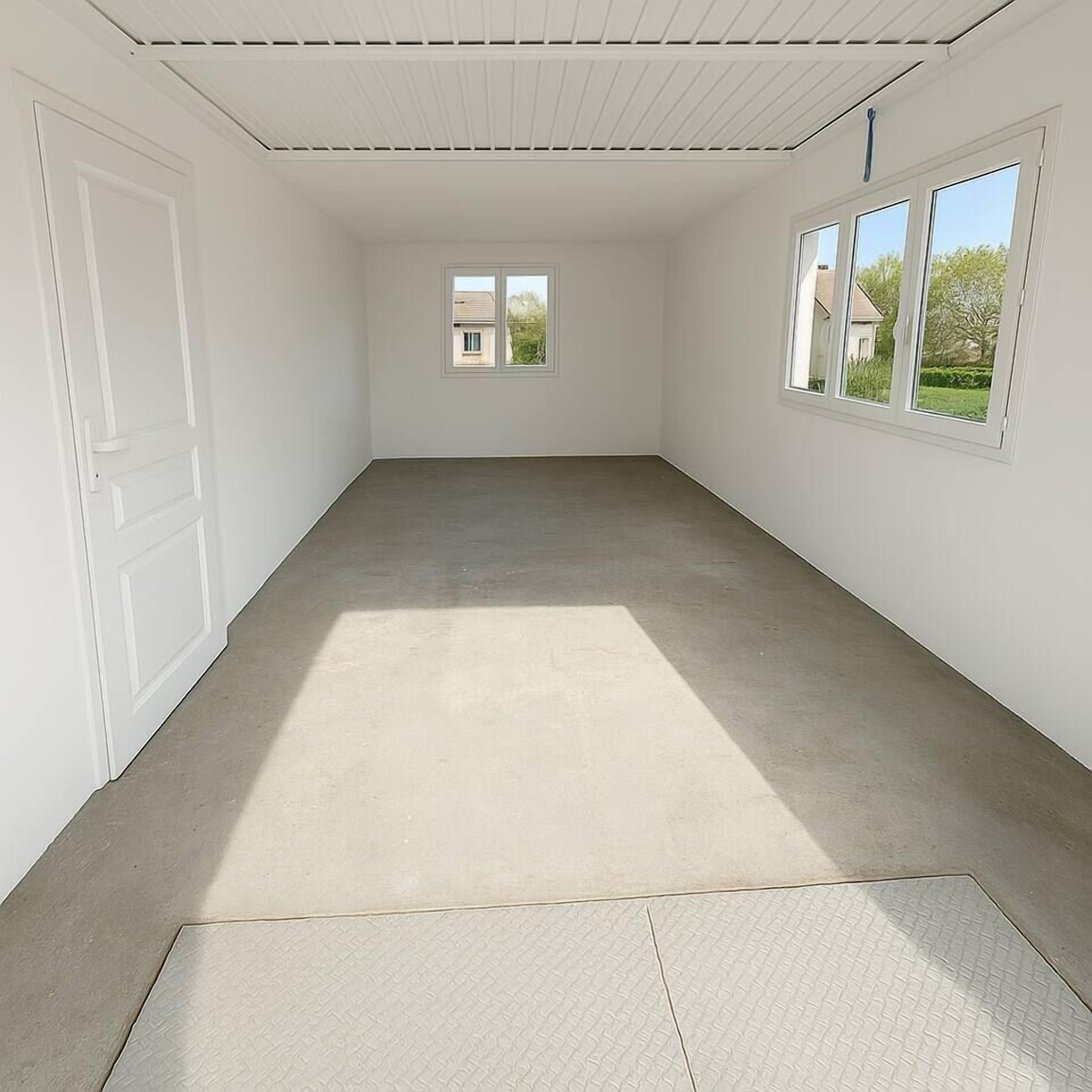 Una habitación con paredes blancas, suelo de concreto y dos ventanas.