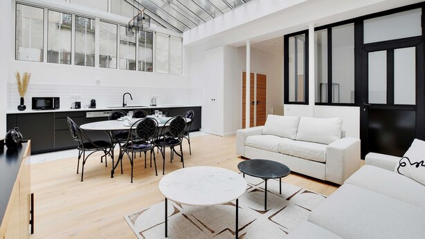 Una cocina moderna con comedor, una sala de estar con sofá y mesa de centro, y un ventanal con vista a la ciudad.